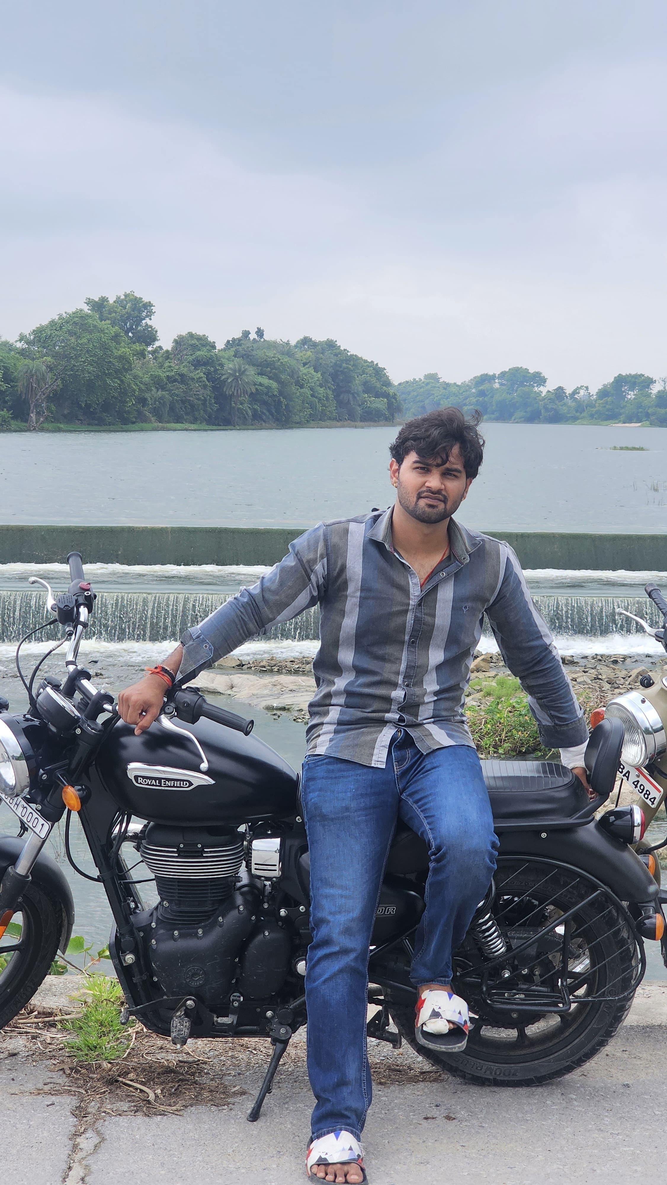 Prince Choudhary seated on a Royal Enfield by a river